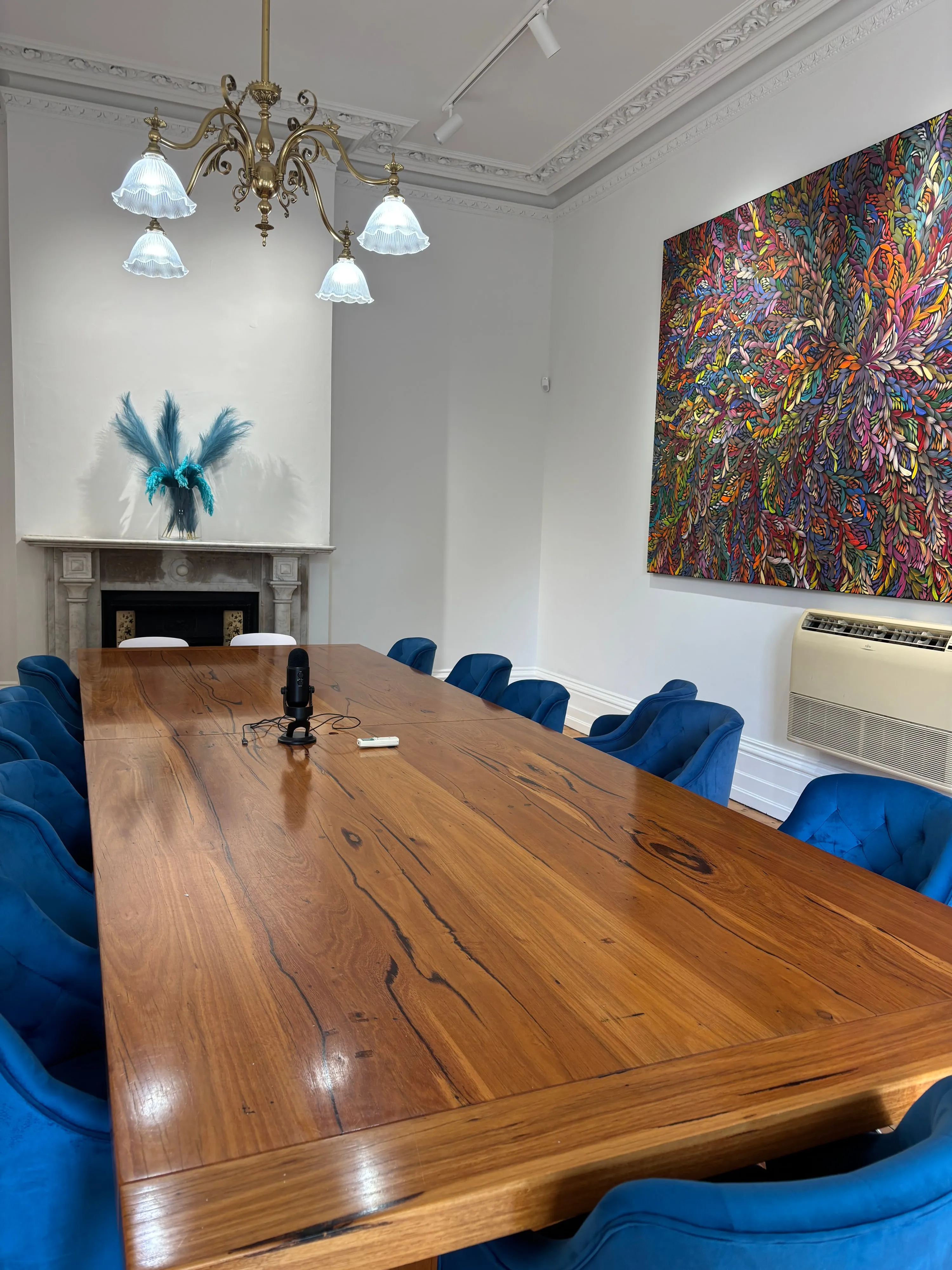 The workshop room at Stanthorpe Mansion, St Kilda — a long timber table with velvet chairs, a marble fireplace and a large contemporary painting